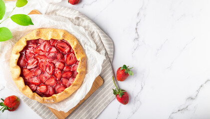 Homemade galette with strawberries on white marble background