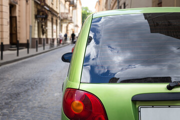 Back window of green car parked on the street in summer sunny day, rear view. Mock-up for sticker...