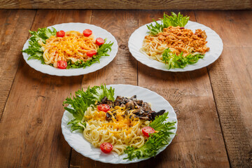 Three plates with different pasta on a wooden table decorated with herbs.