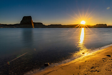 Amanecer  dorarda con rayos del sol sobre el agua sin olas en el desierto en el lago Powell de Utah.