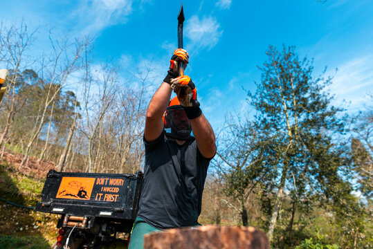  Man in safety equipment cutting wooden logs with axe
