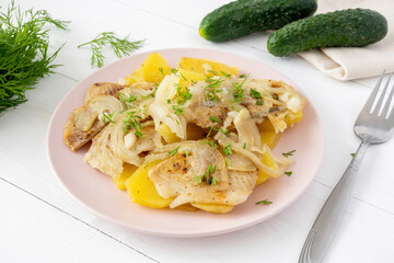 Baked fish and potatoes with onions on the plate on white wooden background. Healthy homemade food made of flounder and vegetables.