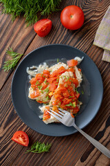 Fish fillet with tomatoes and chopped dill on black plate on wooden table, top view. Backed or stewed flatfish with vegetable garnish for healthy home dinner.