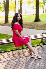 Portrait of a beautiful young girl with long dark wavy hair in a red dress in the park at sunset