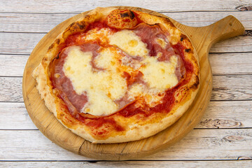 Typical Italian pizza of thin wheat dough with ham and mozzarella cheese gratin