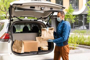 Man by the car. Guy in a delivery uniform. Man in a medical mask. Coronavirus concept.