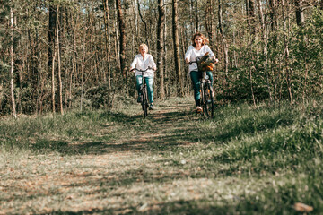 Naklejka premium Two female Mathure friends are riding bicycle bicycles through the forest. Active lifestyle, hobby
