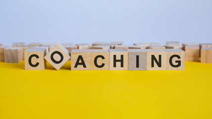 coaching word is made of wooden building blocks lying on the yellow table, concept