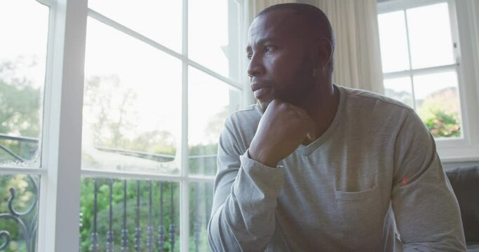 Stressed African American Man Looking Out Of The Window While Sitting On The Couch At Home