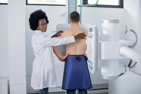 Young African woman doctor radiologist, or x-ray technician, conducting chest x-ray scanning of young male patient in modern examination room
