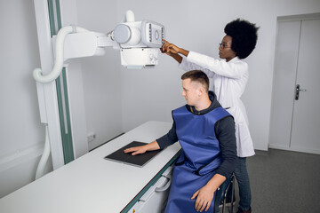 Classic ceiling-mounted x-ray system. Young African woman doctor radiologist and male Caucasian...