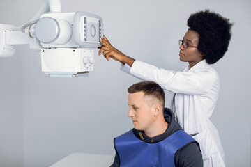 Young afro american female radiologist technician, setting up the modern machine to take x-ray...