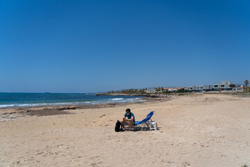 New normal in vacation in time after COVID-19 pandemic. Sad man wearing face mask on beach, sitting on lounge chair and looks out to sea in Cyprus. Male having summer vacation during covid lockdown