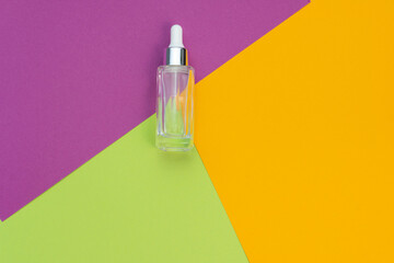 cosmetic flat lay: face serum on a combination of backgrounds green, purple and yellow