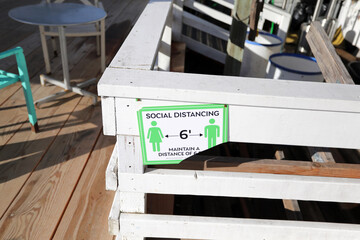 Broken and worn social distancing sign attached to a white railing