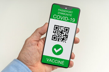 MALE HAND HOLDING A SMARTPHONE AND SHOWING ON THE SCREEN IMMUNITY CERTIFICATE COVID 19 AND VACCINATED IN FRENCH LANGUAGE. DIGITAL PASSPORT BY QR CODE. ESSENTIAL REQUIREMENT FOR TRAVELING.