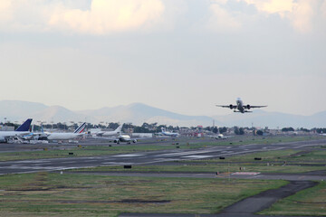 Airplane taking off or landing on runway with blue sky between clouds and mountains
