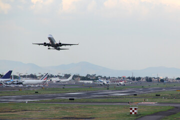 Fototapeta premium Airplane taking off or landing on runway with blue sky between clouds and mountains 