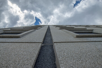 Grey precast concrete exterior cladding panels on a multi-storey building, sky and clouds above,...