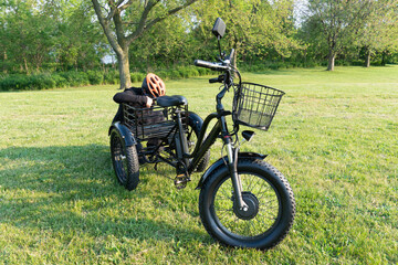 Fototapeta premium Woman in the hamlet hold the key of the electric bicycle battery pack. Female switch on the powered e bike with the key in the park in sunny summer day. The view of the e bike motor.