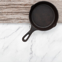 Empty old cast iron skillet set up on white marble  background with flat lay and copy space.