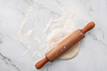 Scattered wheat flour and fresh homemade yeast dough kneaded on marble table with rolling pin on marble table flat lay.