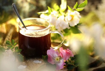 A cup of black coffee in a glass cup. Wooden pad and rose hips. Blurred foreground and background.