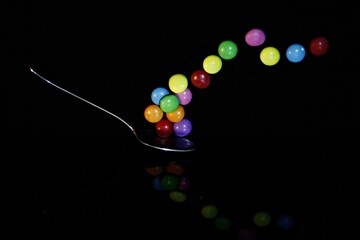 Multicolored candies - lenses - float from the coffee spoon. Black background.