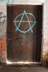 Rusty old metal door of an abandoned building with a blue anarchy symbol