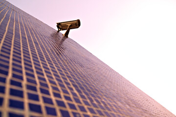 Surveillance camera on the wall of a building, warm subdued evening light.