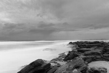 Dramatic grayscale of coastal rocks on background of the sea under the stormy sky