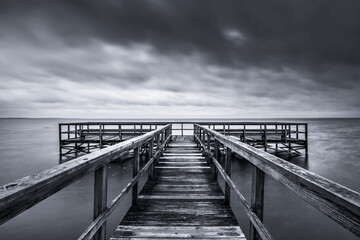 Dramatic grayscale of a weathered pier in the sea on background of the cloudy sky