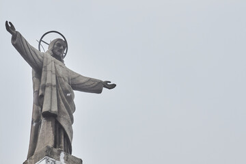 The sculpture of jesus raising his arms in a cloudy weather