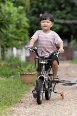 Naklejka premium Asian child on a bike ride in the autumn park. Happy smiling child cycling outdoors. Active lifestyle, hobby