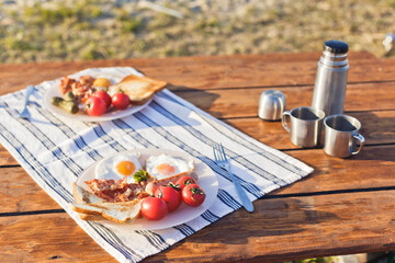 Breakfast in nature. Fried eggs with bacon, fried toast and hot coffee from a thermos