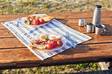 Breakfast in nature. Fried eggs with bacon, fried toast and hot coffee from a thermos