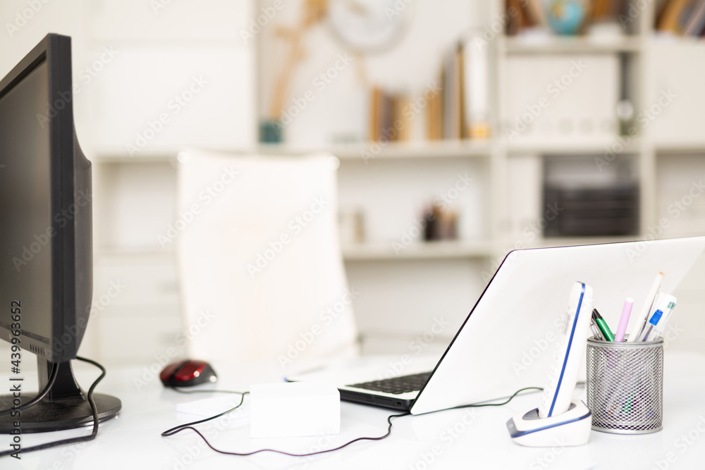 Wall mural Modern equipped workplace for two employees with laptop and desktop computer monitor, telephone and stationery in light empty office