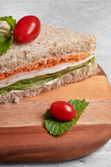 Healthy sandwich with carrots, cheese, lettuce and ham on cutting board.