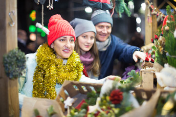 glad family couple with teen daughter choosing Christmas decoration at fair