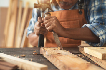 Asian senior carpenters working in the workshop, use a chisel and hammer to carve wood in the...