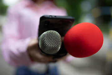 Professional journalist at event, holding microphones and recording notes on smartphone