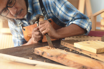 Asian senior carpenters working in the workshop, use a chisel and hammer to carve wood in the workshop, DIY concept