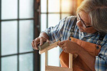 Asian senior carpenter man sanding  a piece of wood in workshop studio, DIY concept © chomplearn_2001