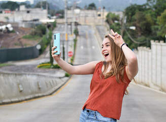 Mujer tomando una foto con el telefono celular, haciendo un gesto de amor y paz a la camara,...