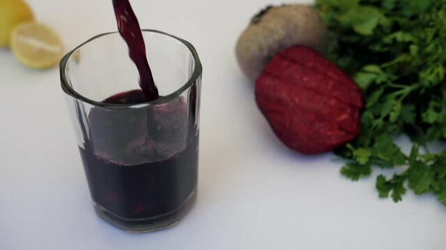 Beetroot juice garnished with mint leaves and slices pouring in a clear glass. Closeup shot of a peeled and unpeeled beetroot  Dhania kept against a white background - healthy food