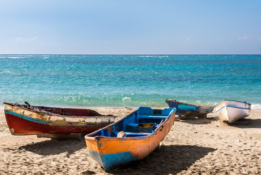 Dramatic image of colorful old wooden weathered fishing boats off the Caribbean coast with turquoise blue water and white sand.