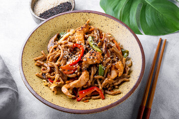 Plate of asian buckwheat soba noodles with vegetables, mushrooms and chicken on light gray background close up