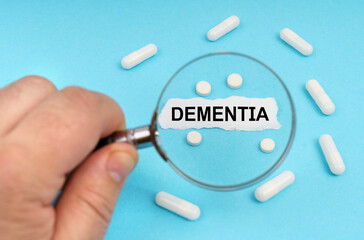 A man looks through a magnifying glass at pills and a leaf with the inscription - DEMENTIA