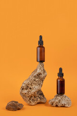 Serum or essential oil in brown glass dropper bottle on stones, orange background. Natural Organic Spa Cosmetic concept Front view