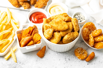 Chicken nuggets, strips, french fries, fried potatoes, ketchup and cheese sauce on a light background. Fast food closeup
